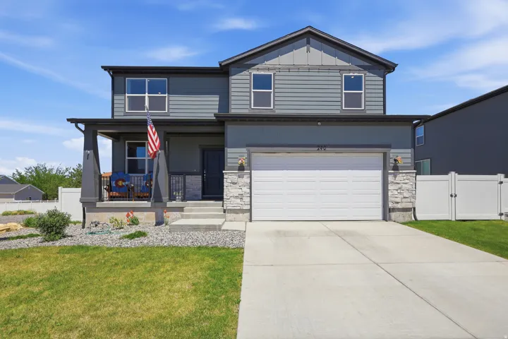 Two-story residence featuring a covered front porch, an attached garage, a concrete driveway, a white vinyl fence, and a landscaped front yard with grass and decorative rock