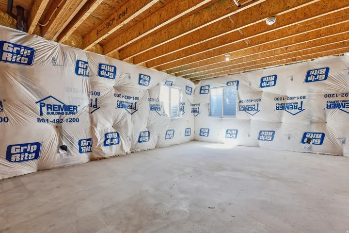 Unfinished room featuring exposed ceiling joists, concrete flooring, insulated walls, and two windows