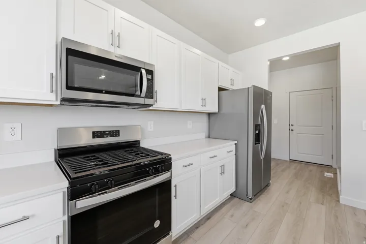 White shaker-style cabinetry, stainless steel appliances, light-toned wood-finish flooring, recessed ceiling lighting, and solid surface countertops