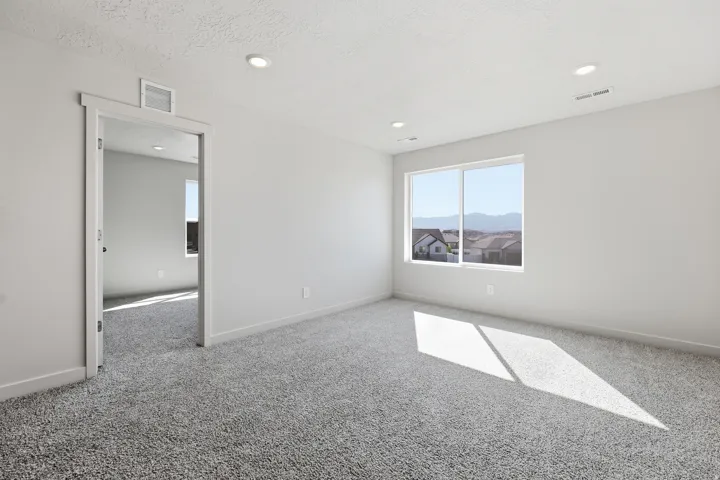 Plush grey carpeting, white painted walls, recessed ceiling lighting, and a large window with a white frame