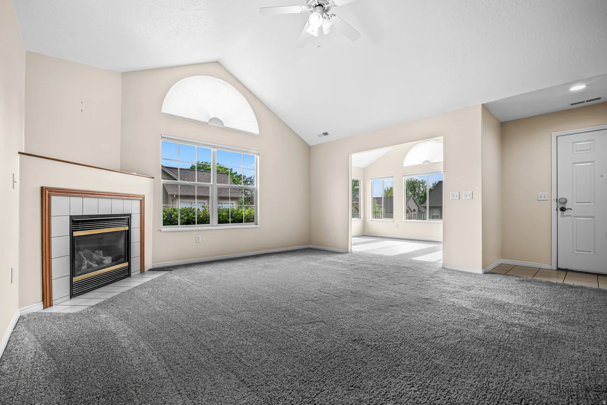 Living room with vaulted ceiling, arched transom window, and a fireplace featuring a white tile surround and wood-finish mantel