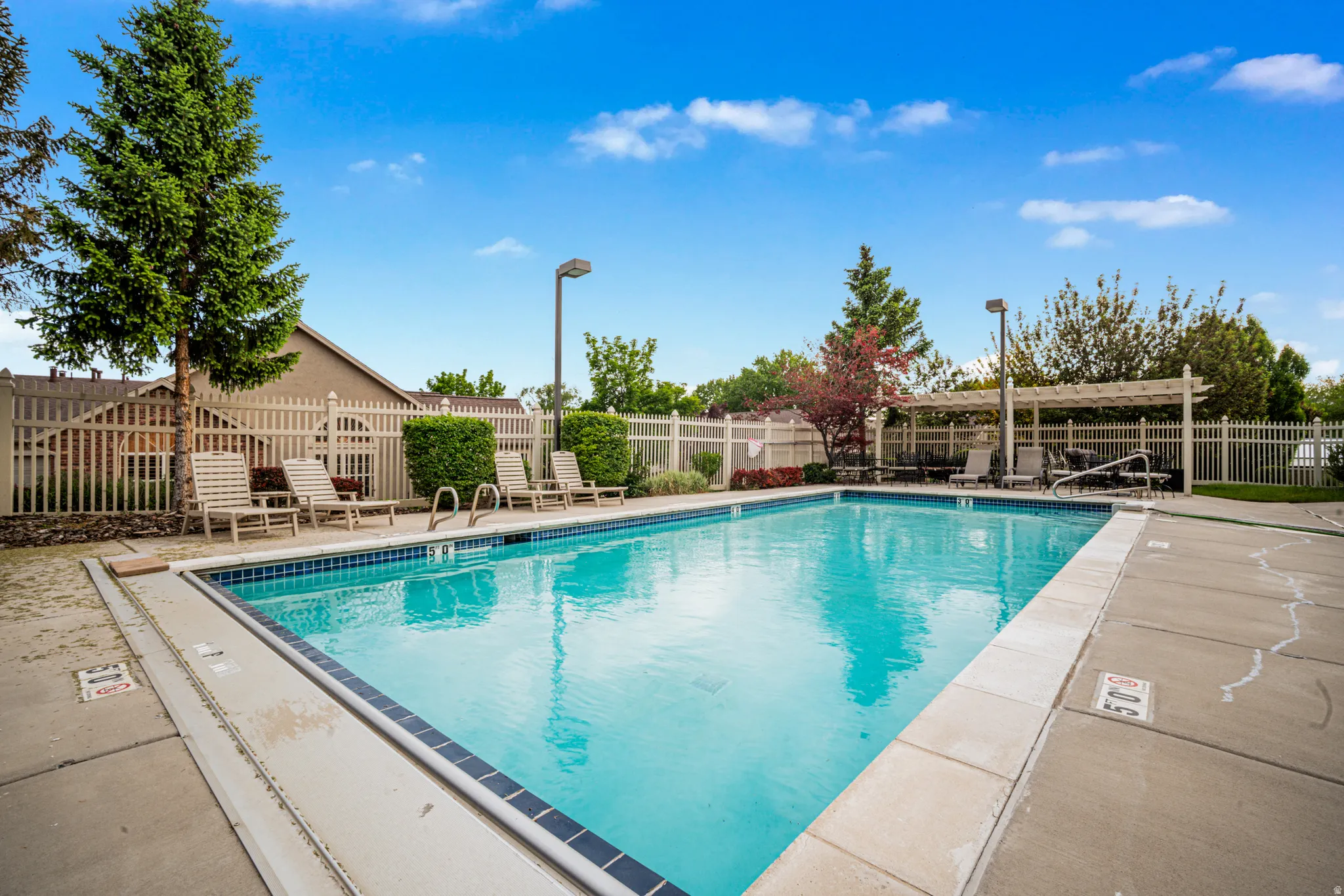Community outdoor swimming pool featuring a concrete deck surround, blue tile accents, and an adjacent pergola-covered seating area