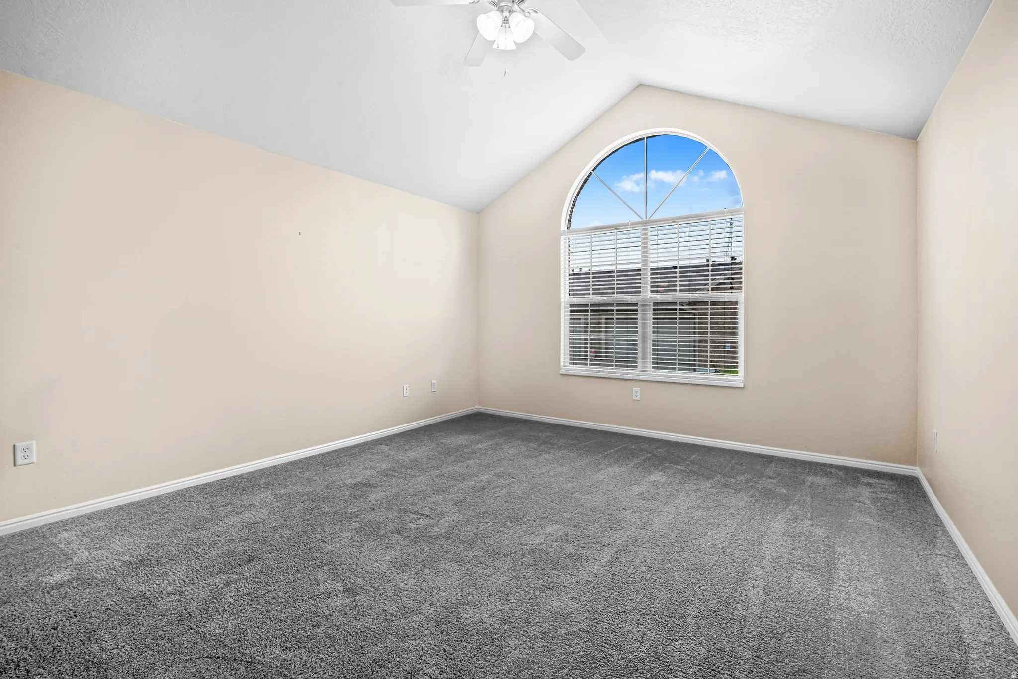 Bedroom featuring a large arched window with blinds, vaulted ceilings, a ceiling fan, and grey carpeting