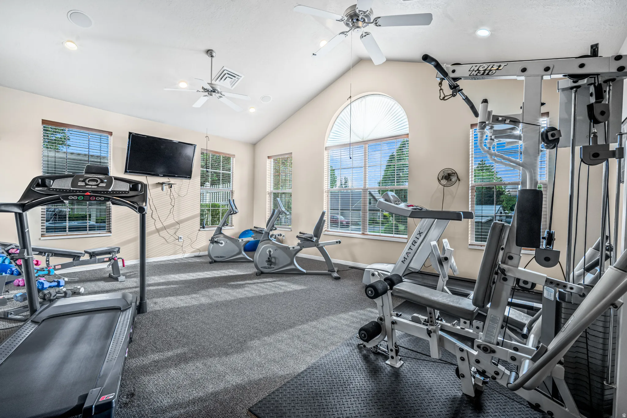 Fitness area featuring vaulted ceilings, recessed lighting, and multiple windows with blinds