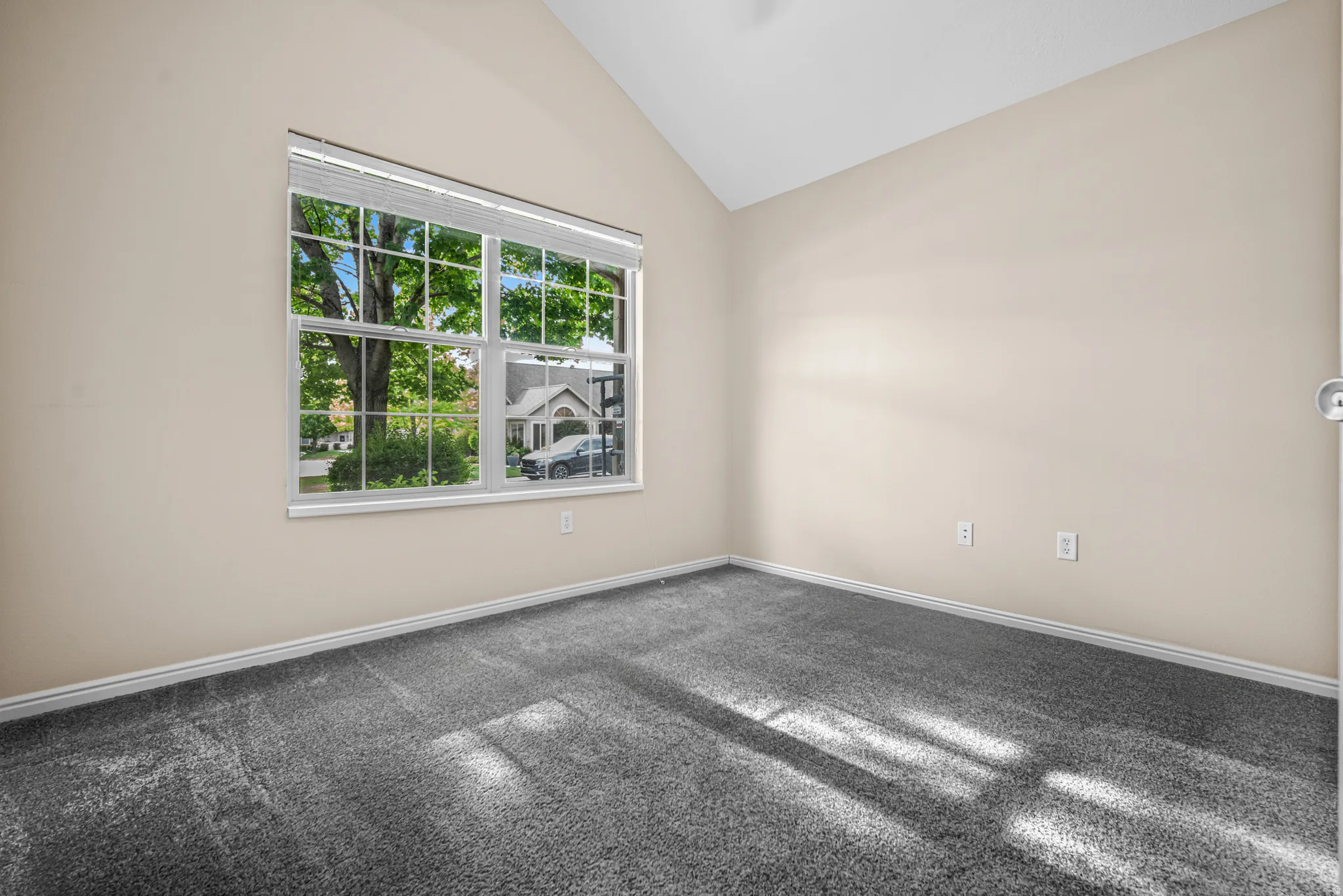 Vaulted ceiling room featuring a large window with white blinds, neutral wall paint