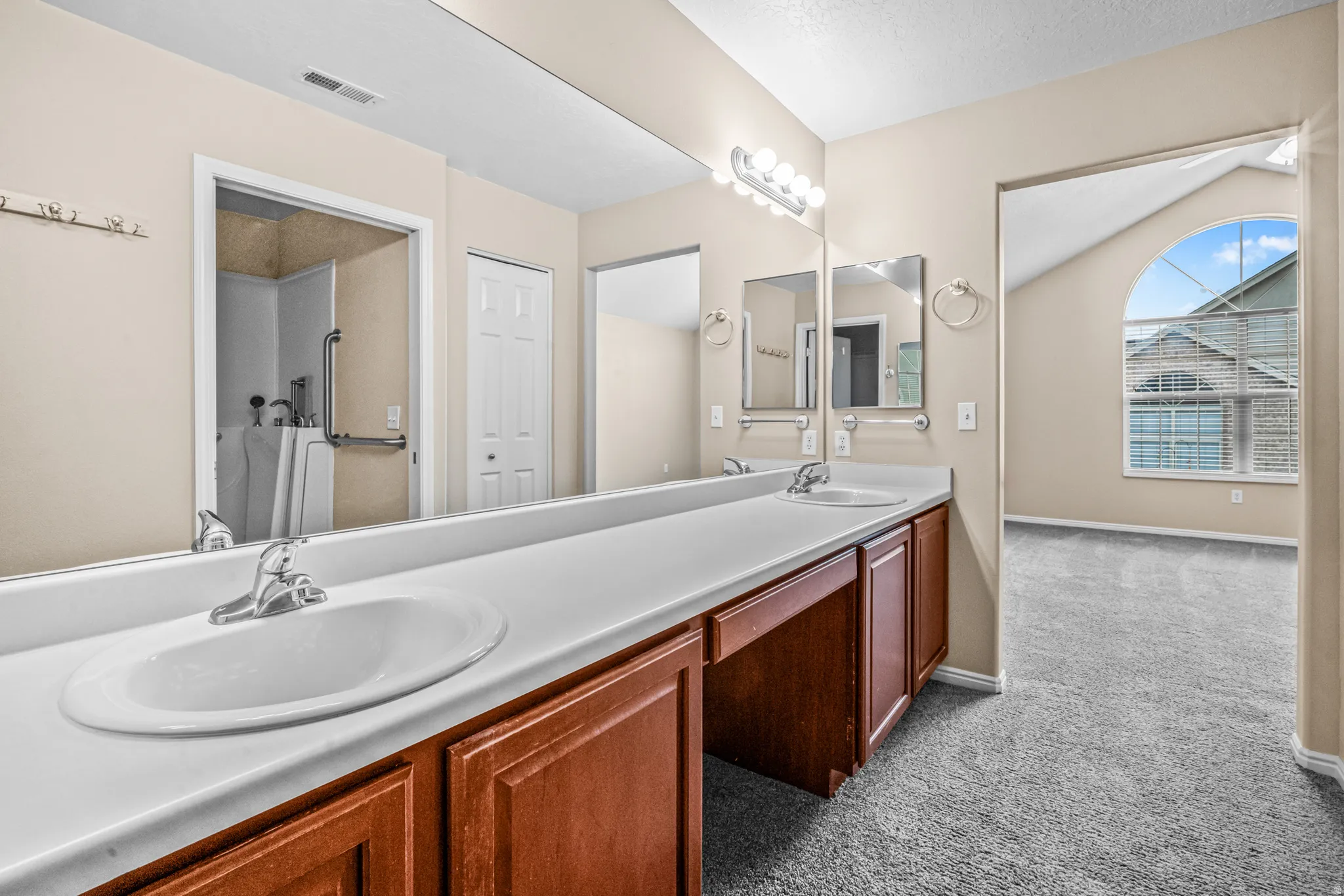 Extended vanity with dual sinks, ample countertop space, wood-finish cabinetry, and overhead bar lighting