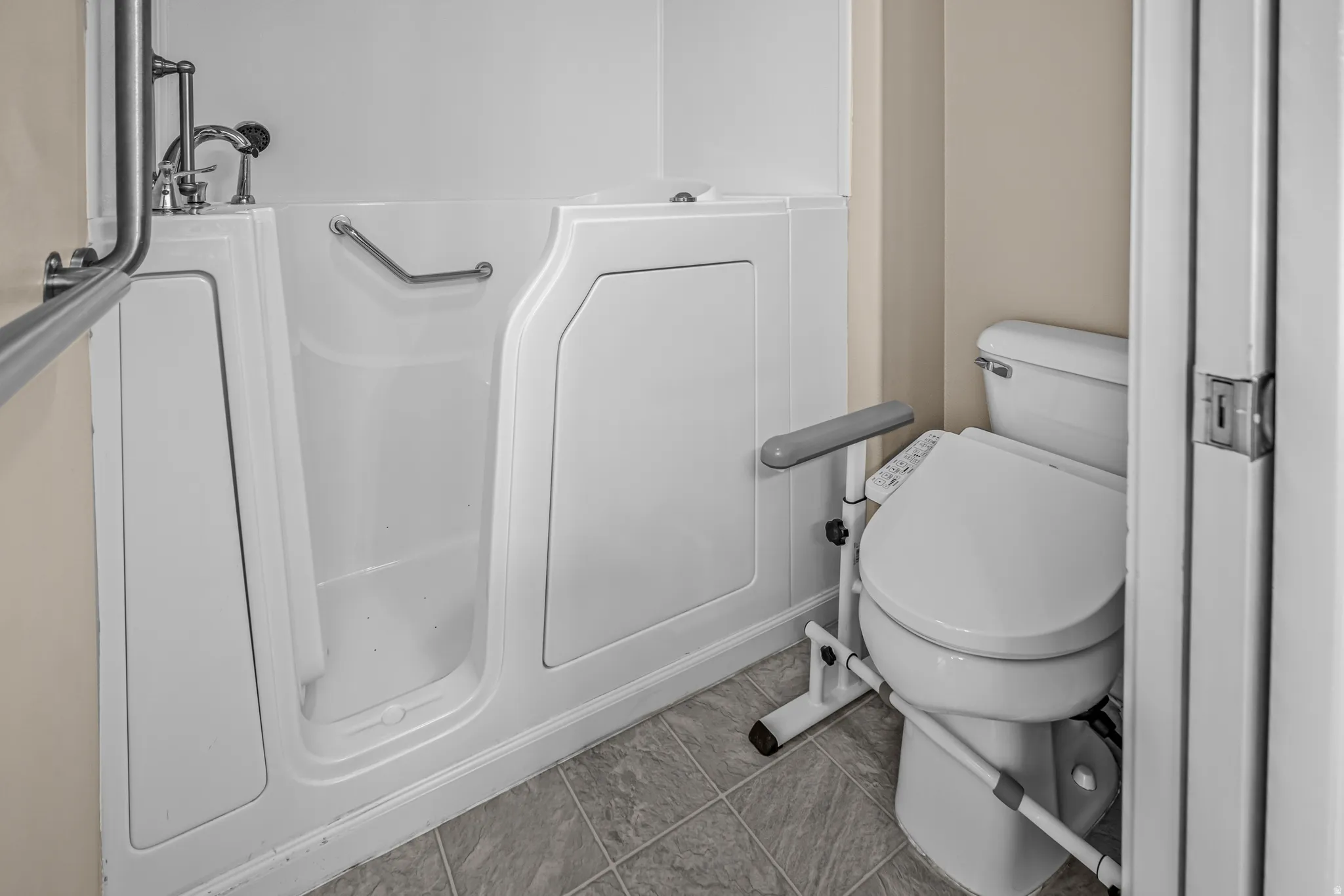 Bathroom featuring a walk-in tub with grab bars and chrome fixtures, alongside a toilet with a bidet attachment