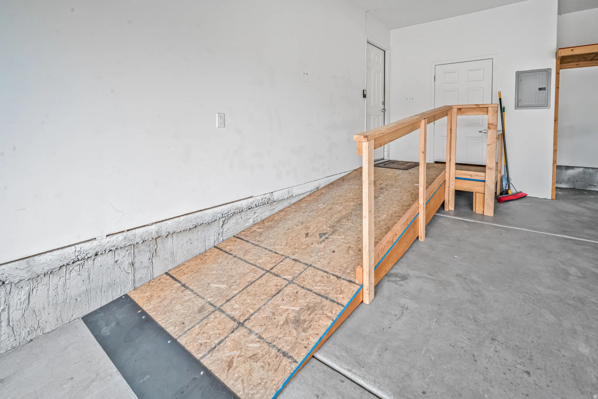 Garage interior featuring a built-in wooden ramp with handrails, concrete flooring, and white painted walls.  Ramp can be easily removed.