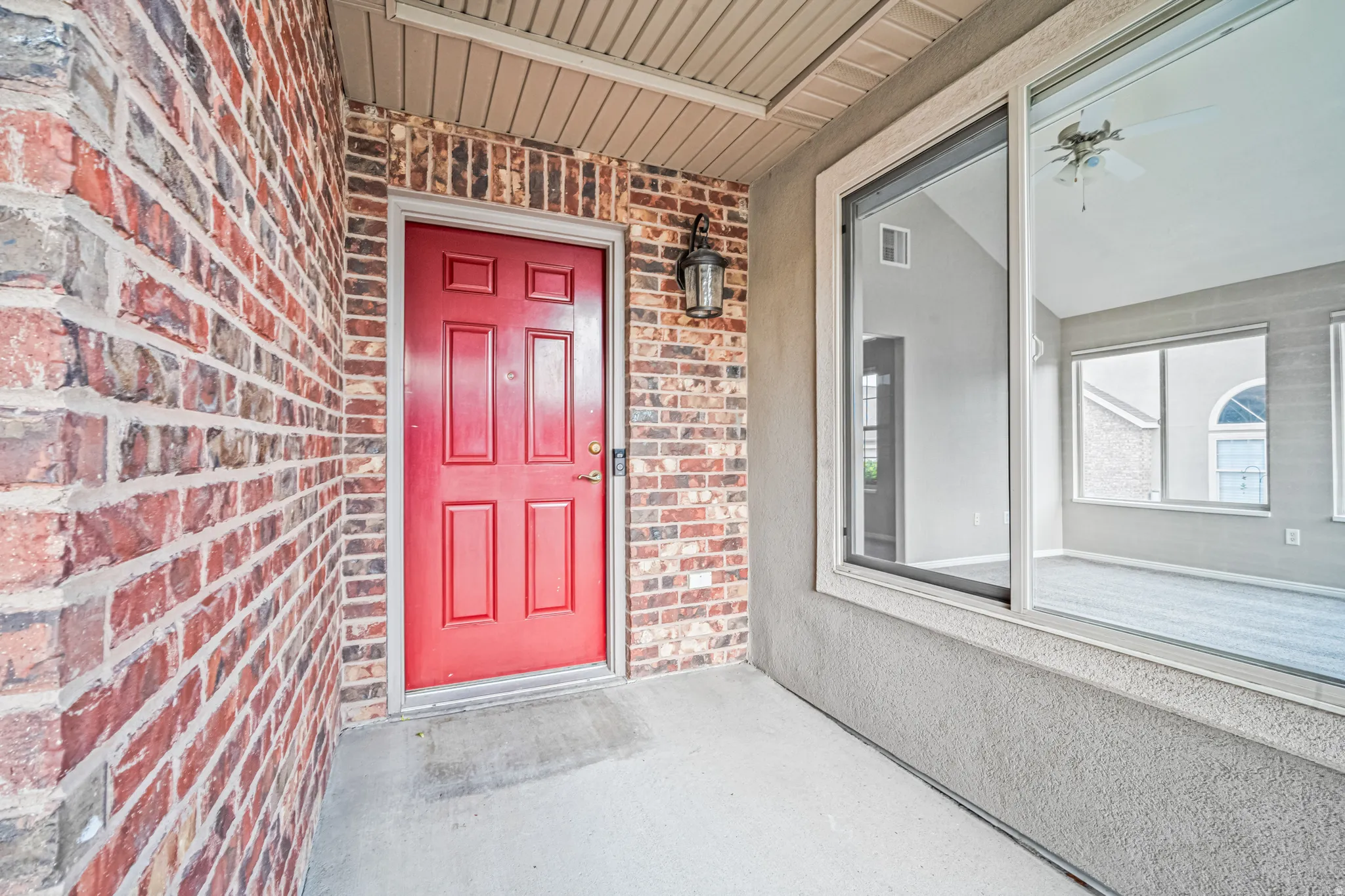 Red panel door entry with brick facade, stucco exterior, and an overhead porch light fixture