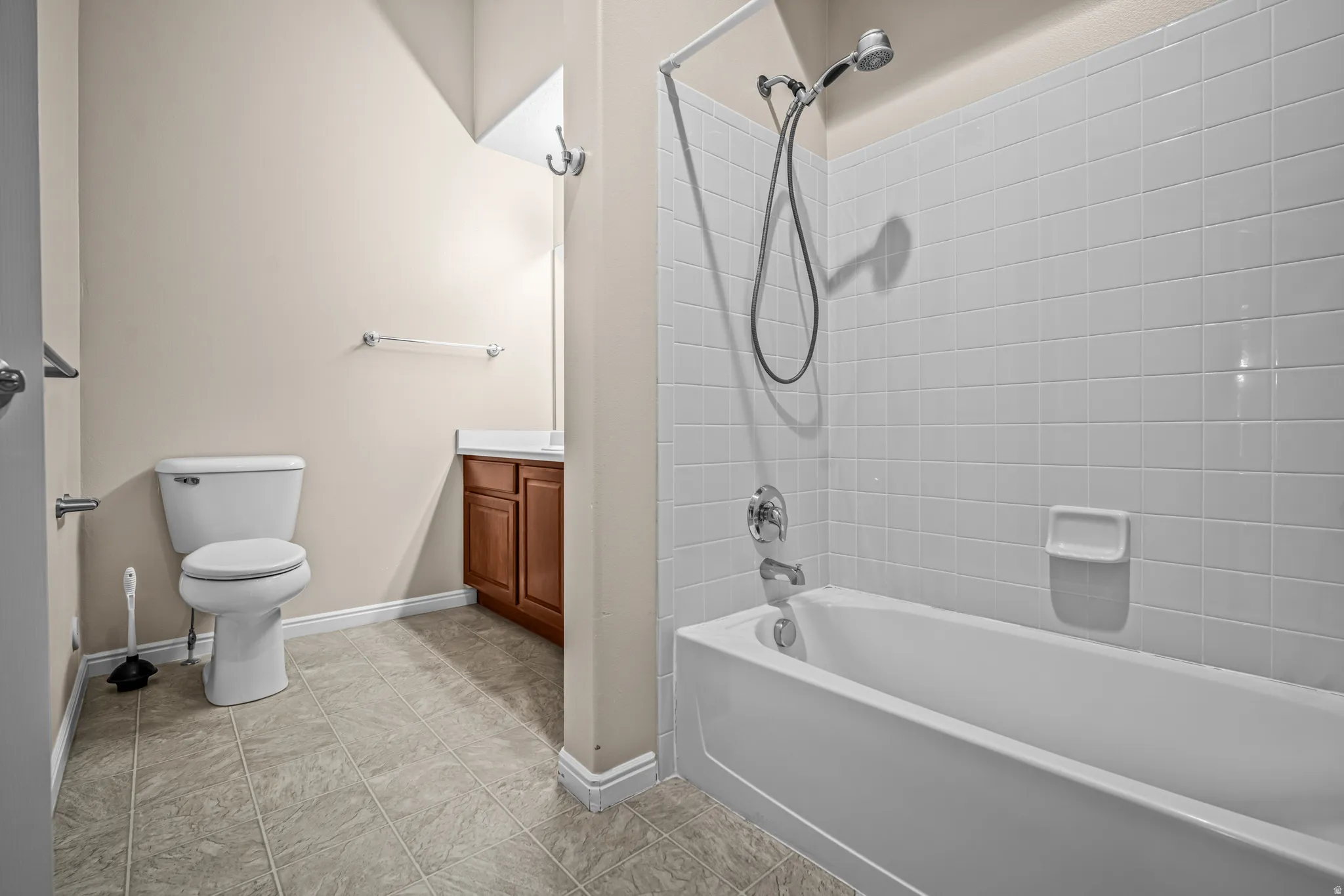 Bathroom featuring a white bathtub with tile surround, shower fixture, and a wood-finish vanity
