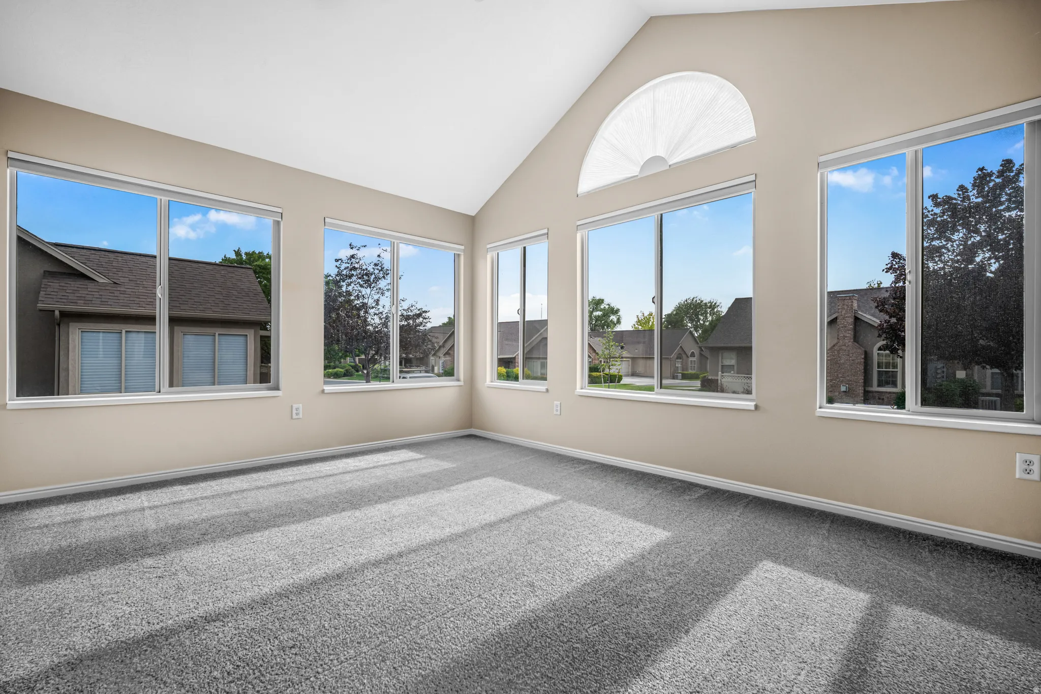 Vaulted ceiling sunroom featuring multiple large windows, an arched transom window, neutral wall tones