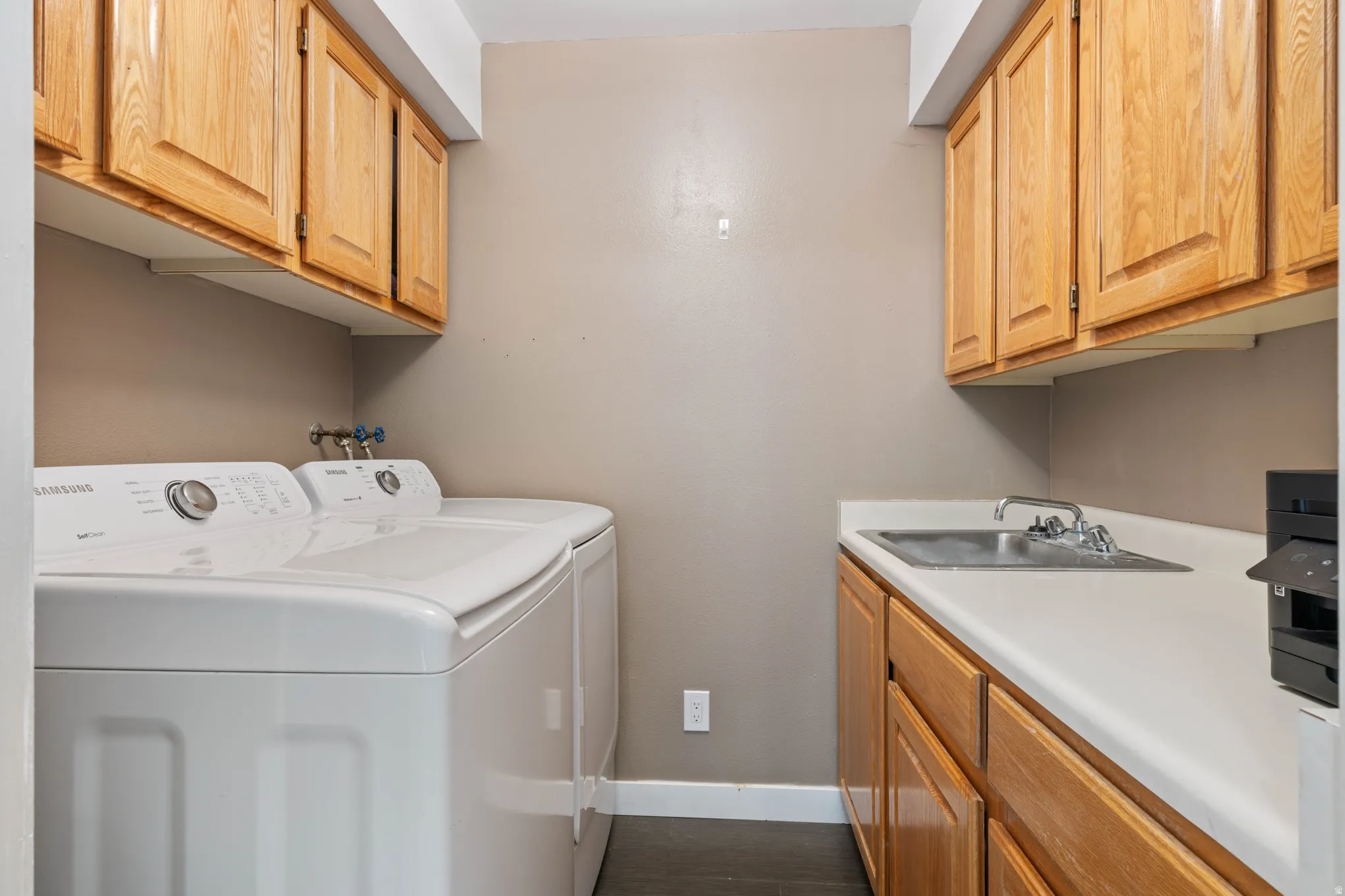 Dedicated laundry area featuring wood-finish cabinetry, a utility sink with a chrome faucet, and white countertops