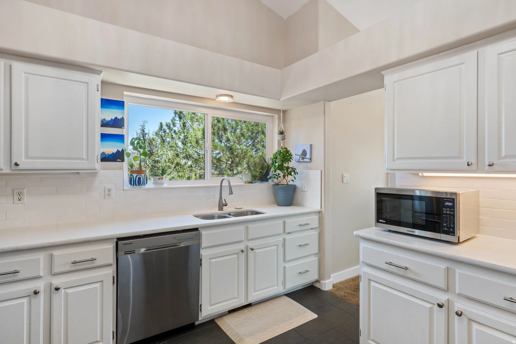 Kitchen featuring white shaker-style cabinetry, a double basin stainless steel sink, light-toned countertops, and a subway tile backsplash