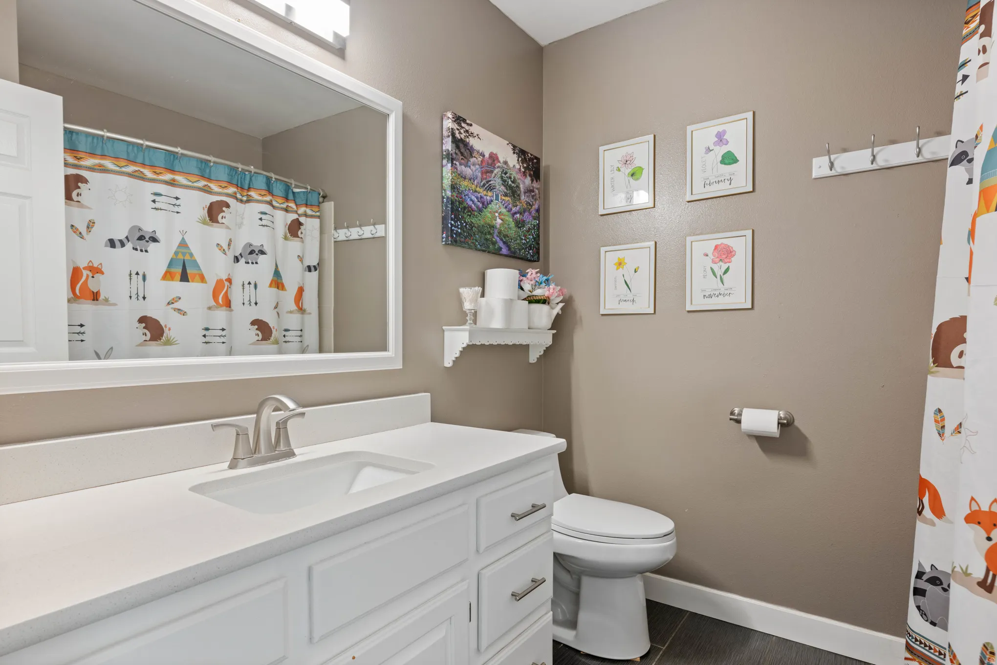Bathroom featuring a white vanity with an integrated sink, brushed nickel faucet, large framed mirror, and dark tile flooring