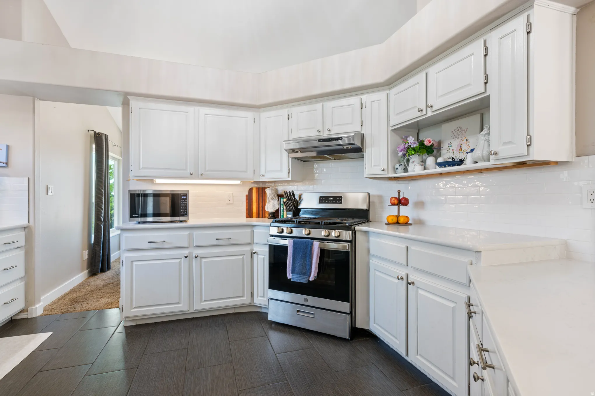 Kitchen featuring white shaker-style cabinetry, white subway tile backsplash, stainless steel range with overhead microwave, white countertops, and dark tile flooring