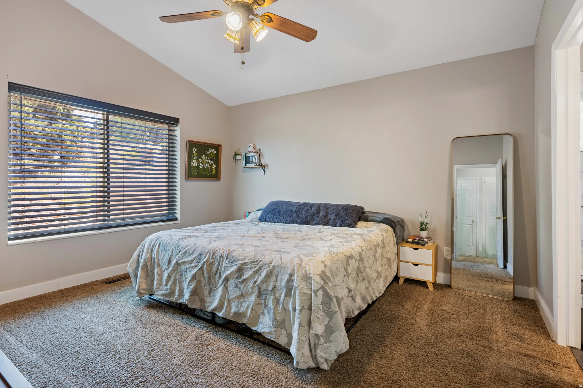 Carpeted room featuring a vaulted ceiling and a wood-finish ceiling fan with integrated lighting