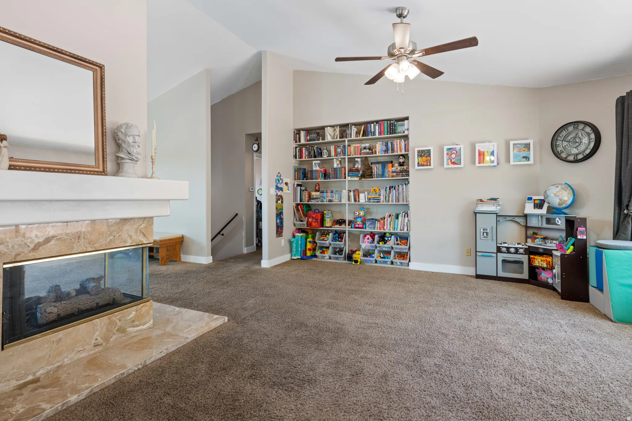 Spacious living area featuring a corner fireplace with stone surround, a built-in shelving unit, a ceiling fan, and vaulted ceilings