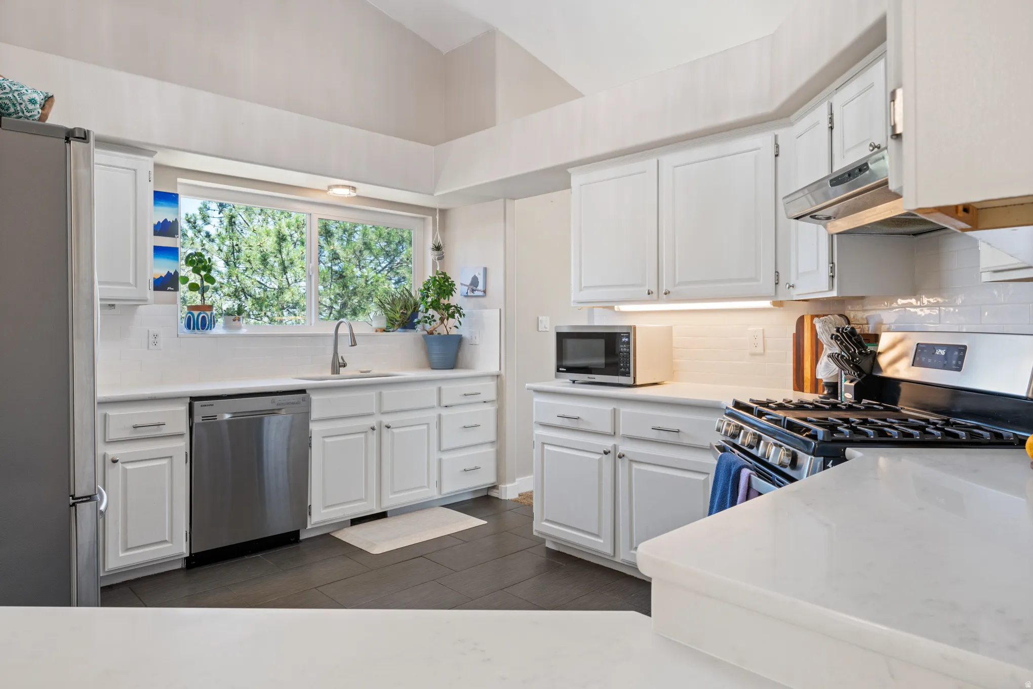 Kitchen featuring white cabinetry, light countertops, subway tile backsplash, and dark tile flooring