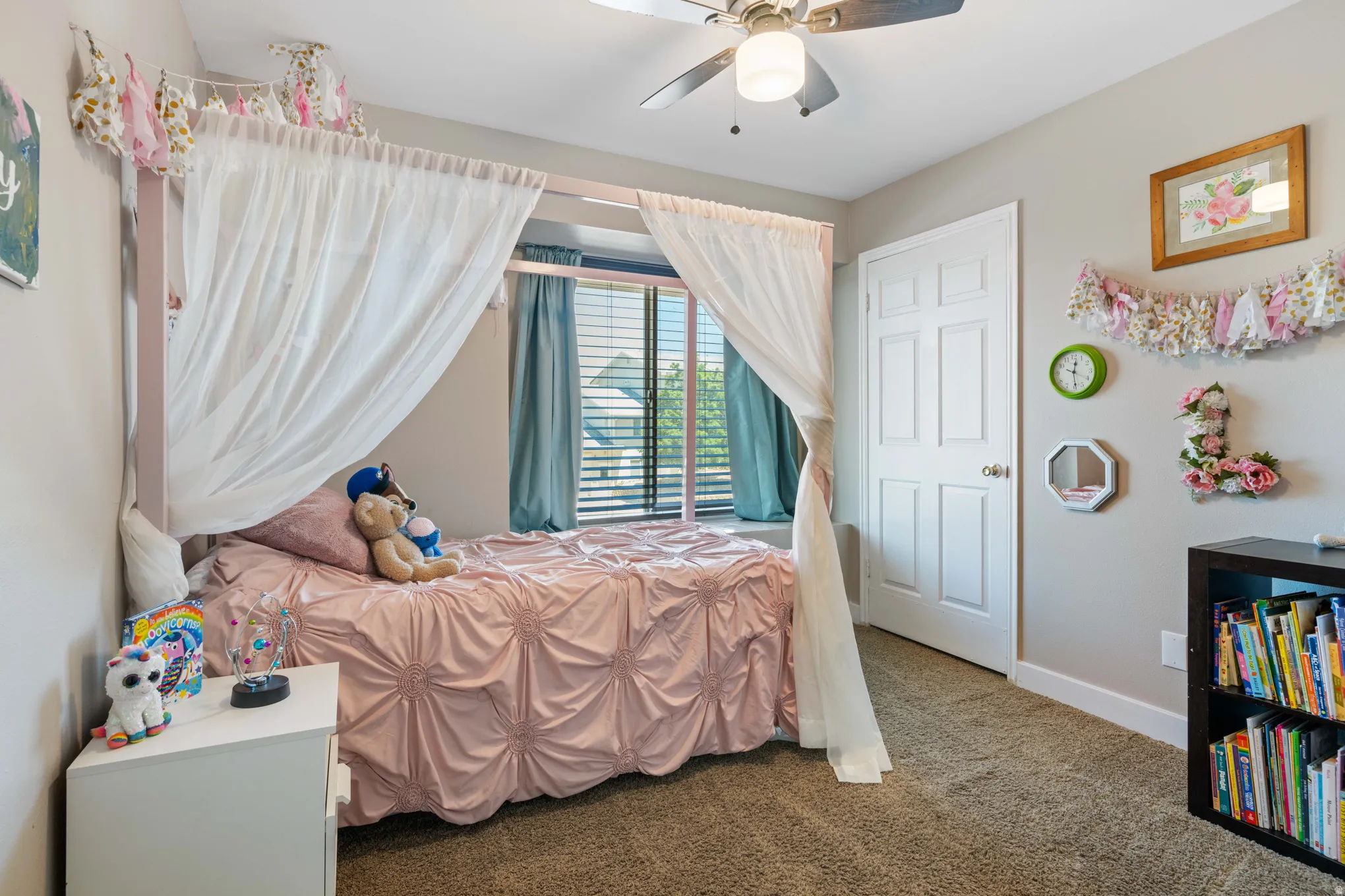 Carpeted room featuring a ceiling fan with integrated lighting, a white six-panel door, and a window with blinds and blue drapery