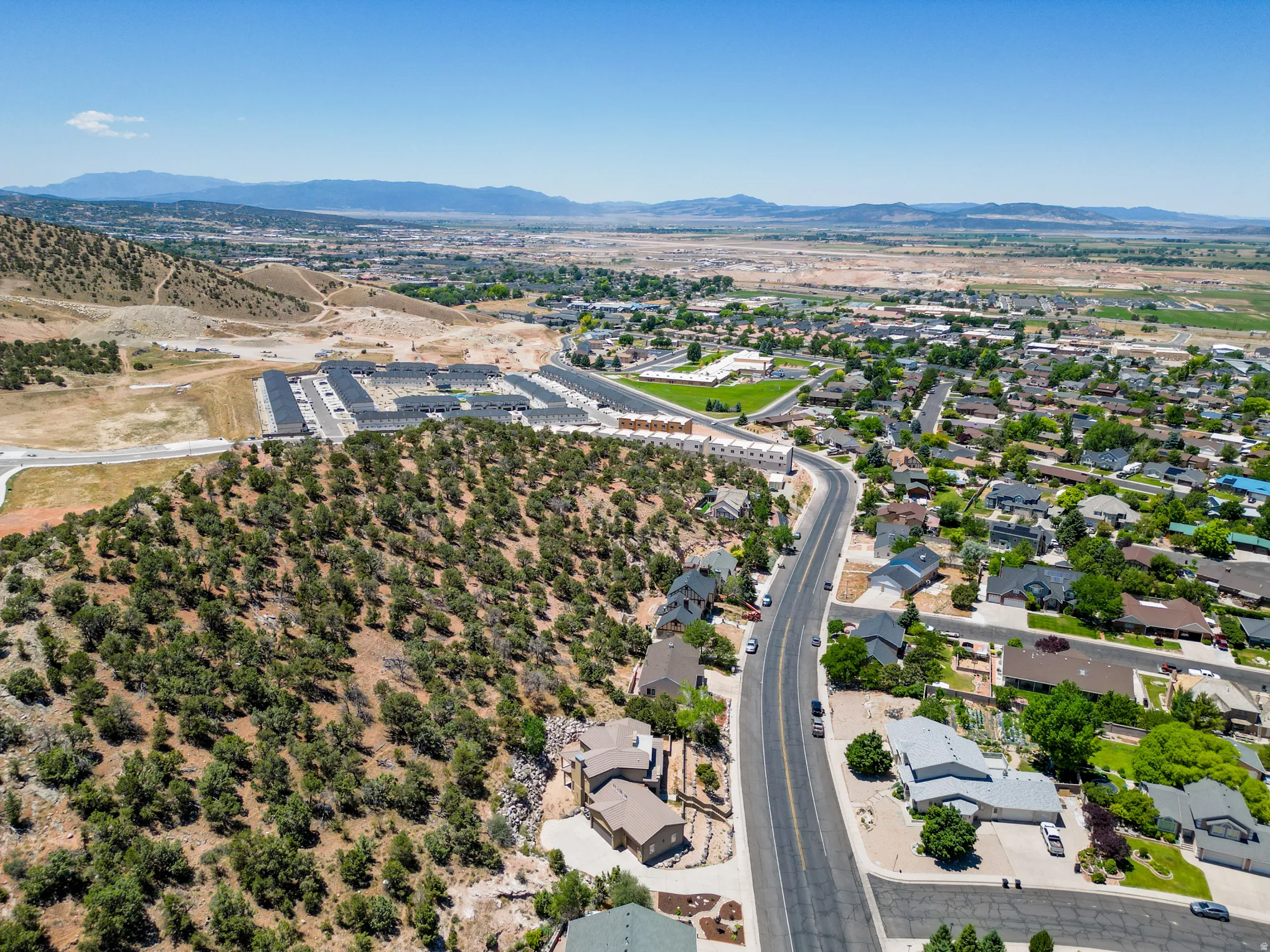Expansive aerial perspective showcasing varied residential developments, a winding road, and natural landscapes