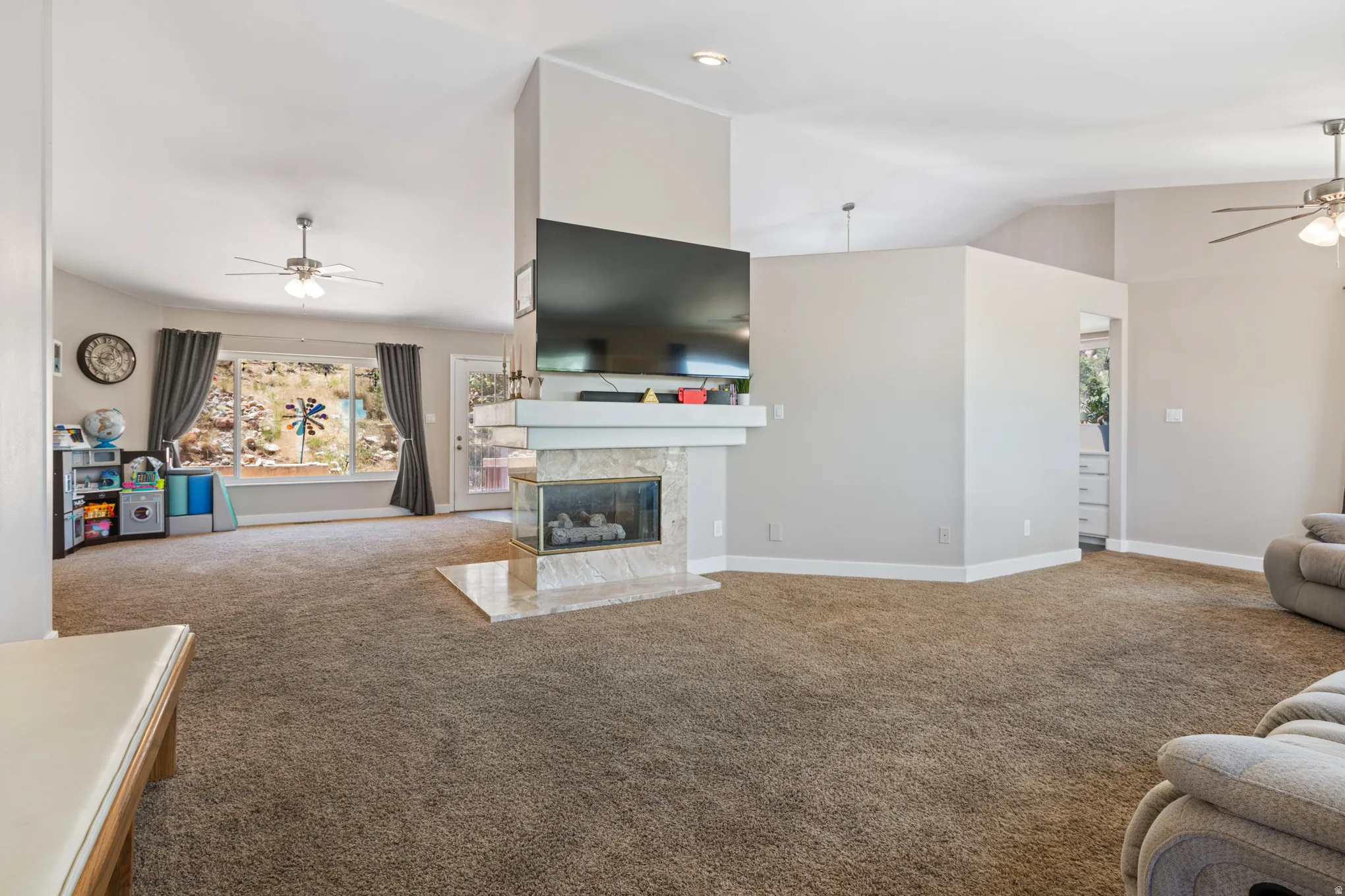 Spacious living area featuring a central fireplace with stone-look tile surround and a white mantel, vaulted ceilings, and a large bay window