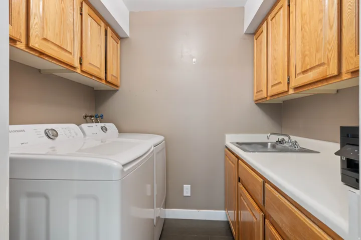 Dedicated laundry area featuring wood-finish cabinetry, a utility sink with a chrome faucet, and white countertops