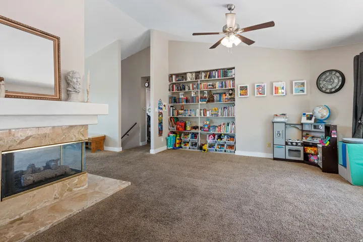 Spacious living area featuring a corner fireplace with stone surround, a built-in shelving unit, a ceiling fan, and vaulted ceilings