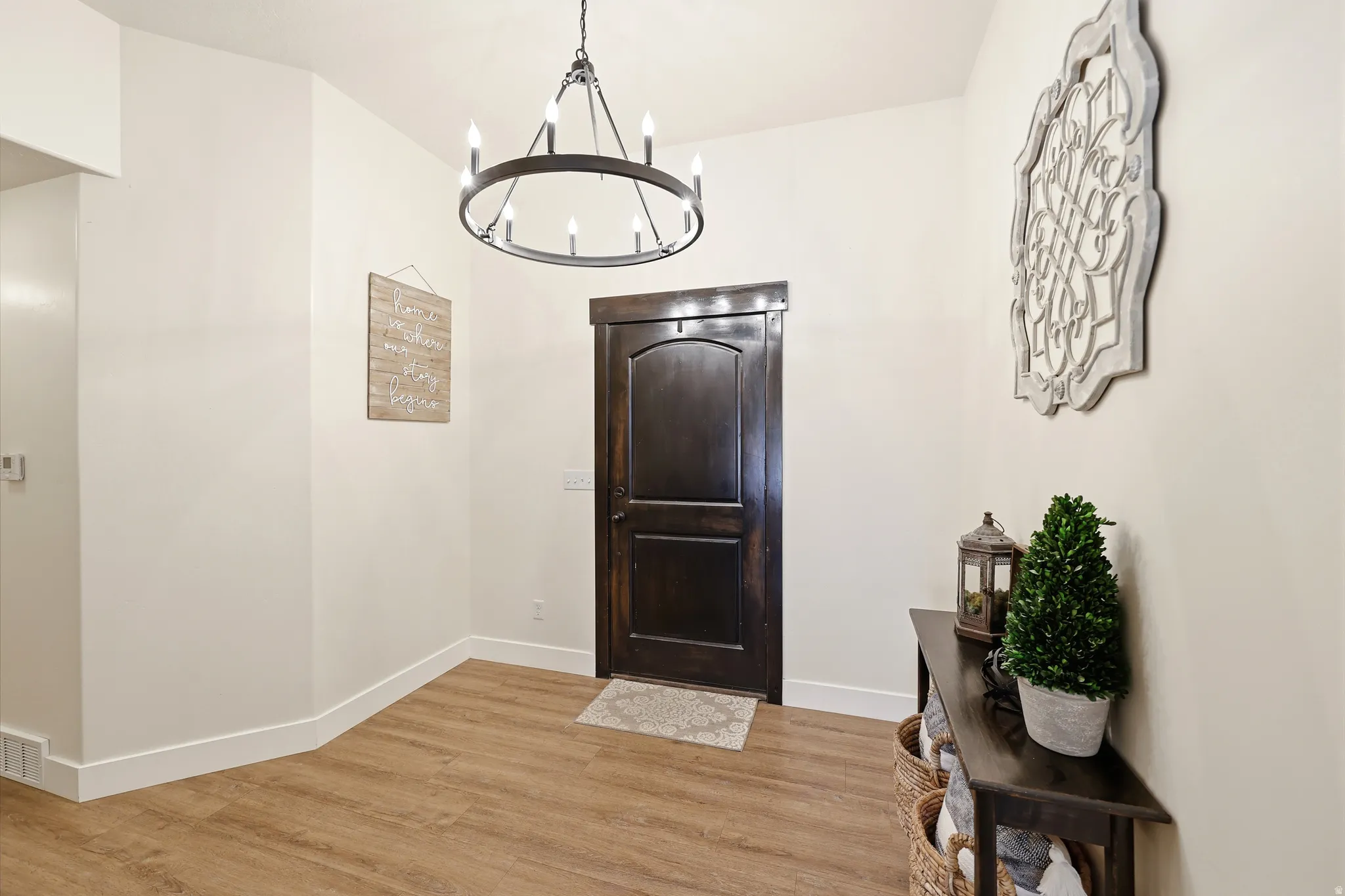 Entryway featuring wood-finish flooring, a dark wood-paneled door with trim, and a prominent circular chandelier