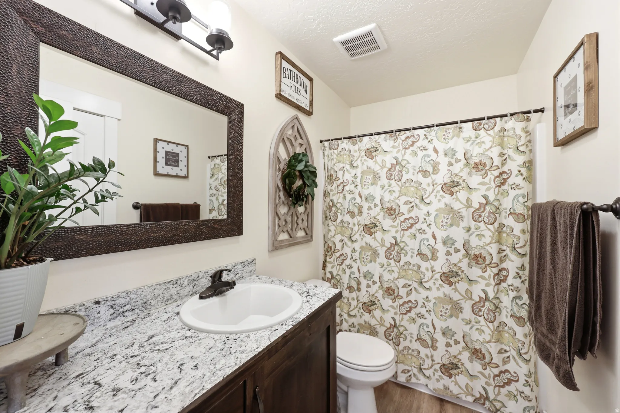 Bathroom featuring a dark wood-finish vanity with a white oval sink, speckled countertop, and a dark-framed mirror