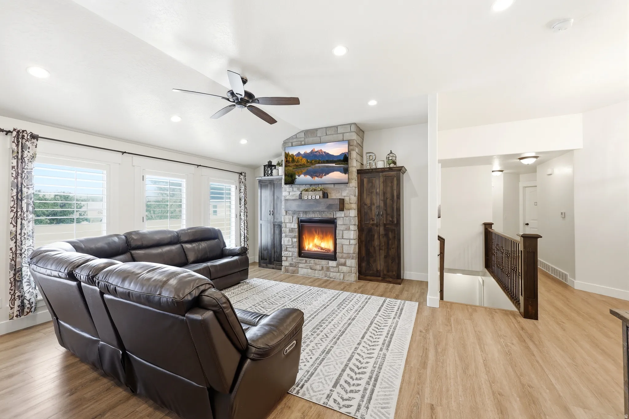Living area featuring a stone-clad fireplace with a wood mantel, vaulted ceiling with a ceiling fan, recessed lighting, and wood-finish flooring