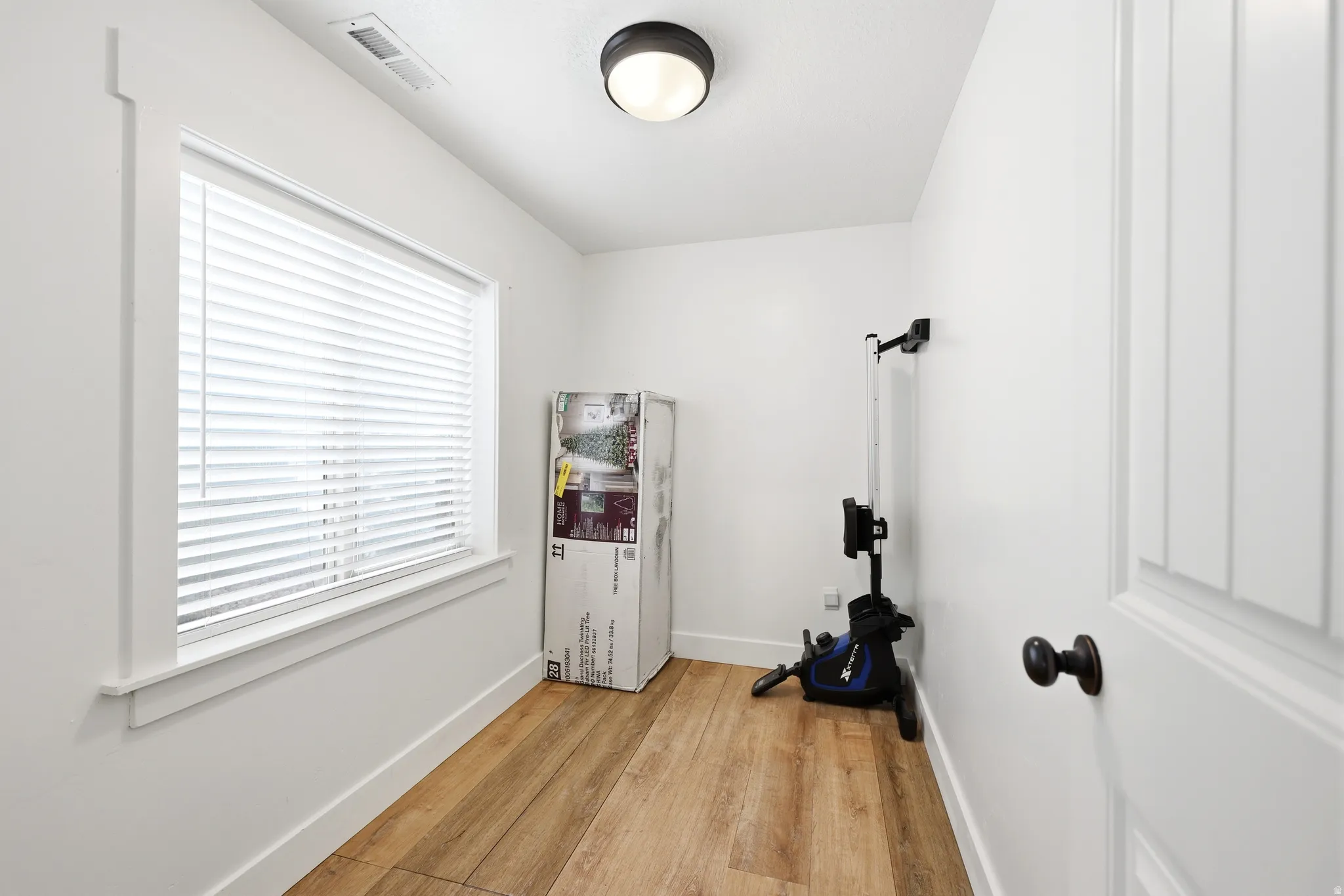 Bright room featuring wood-finish flooring, a contemporary ceiling light fixture, and a window with blinds