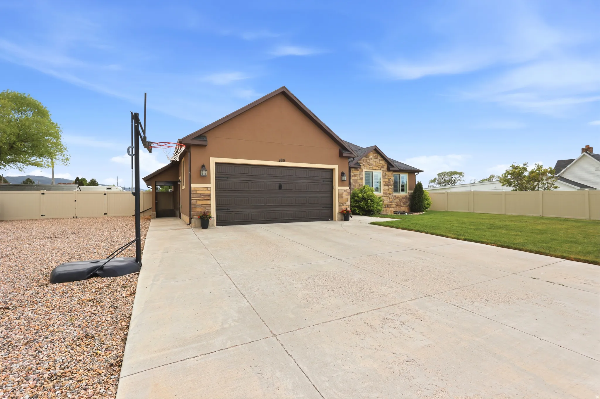 Exterior featuring stucco and stone accents, an attached garage, a concrete driveway, a manicured lawn, and a vinyl fence