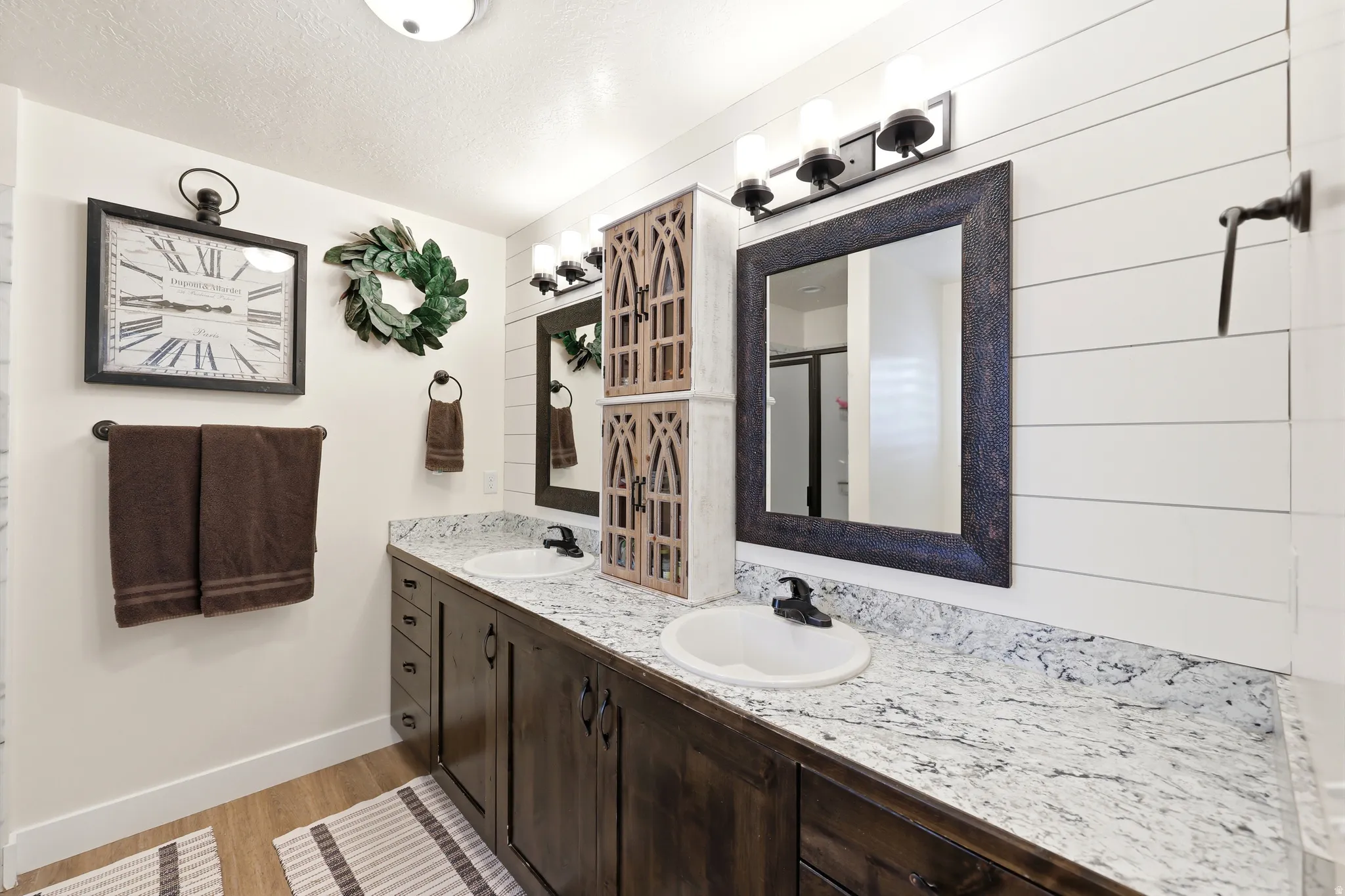 Dual vanity with granite-style countertop, undermount sinks, wood-finish cabinetry, and matte black fixtures