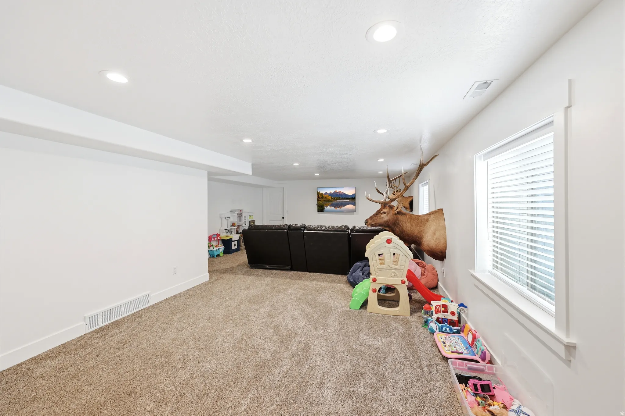 Spacious carpeted room featuring recessed lighting, white walls, and a window with blinds