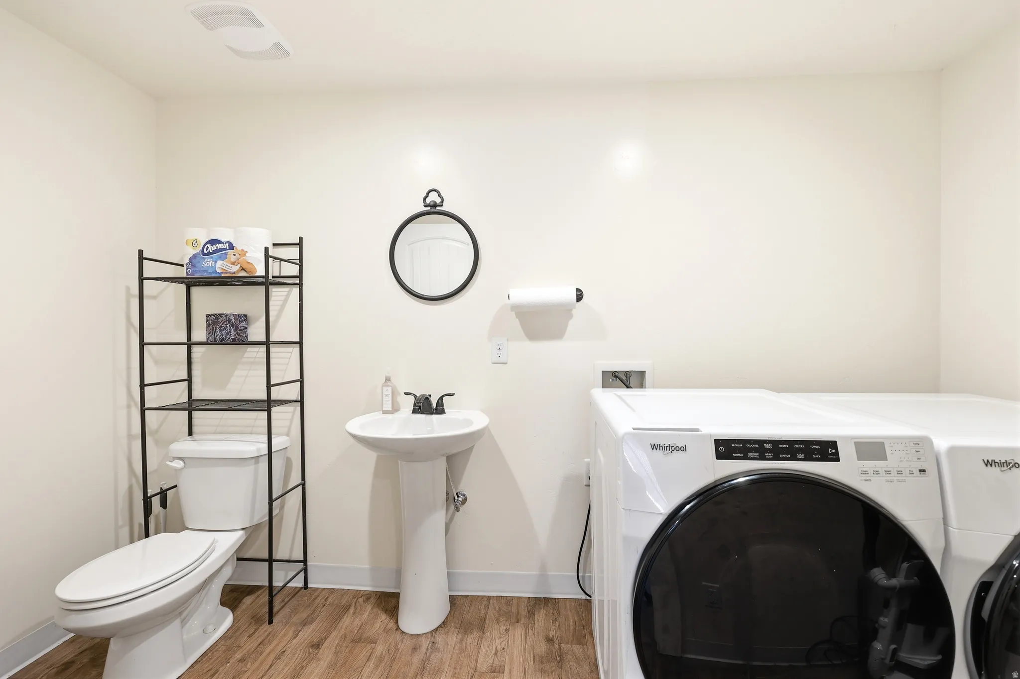 Laundry area featuring wood-finish flooring, a white pedestal sink with a black faucet, and a contemporary toilet
