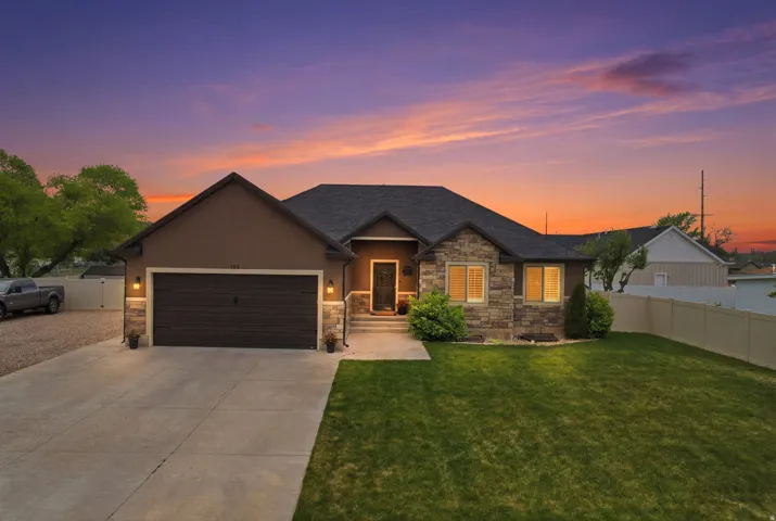 Exterior featuring a two-car garage, stone and stucco facade, concrete driveway, and front lawn