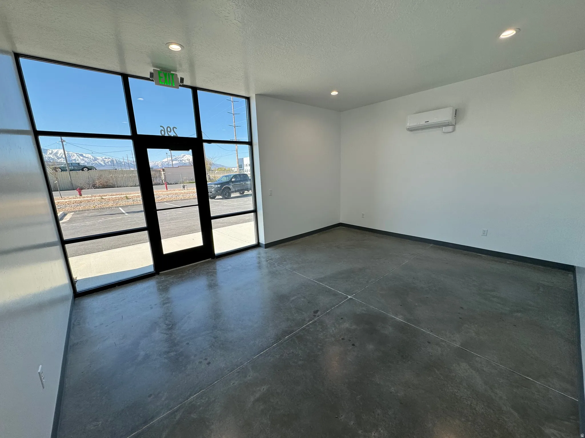 Commercial space featuring expansive glass frontage with a central door, polished concrete flooring, recessed lighting, and a wall-mounted mini-split HVAC system