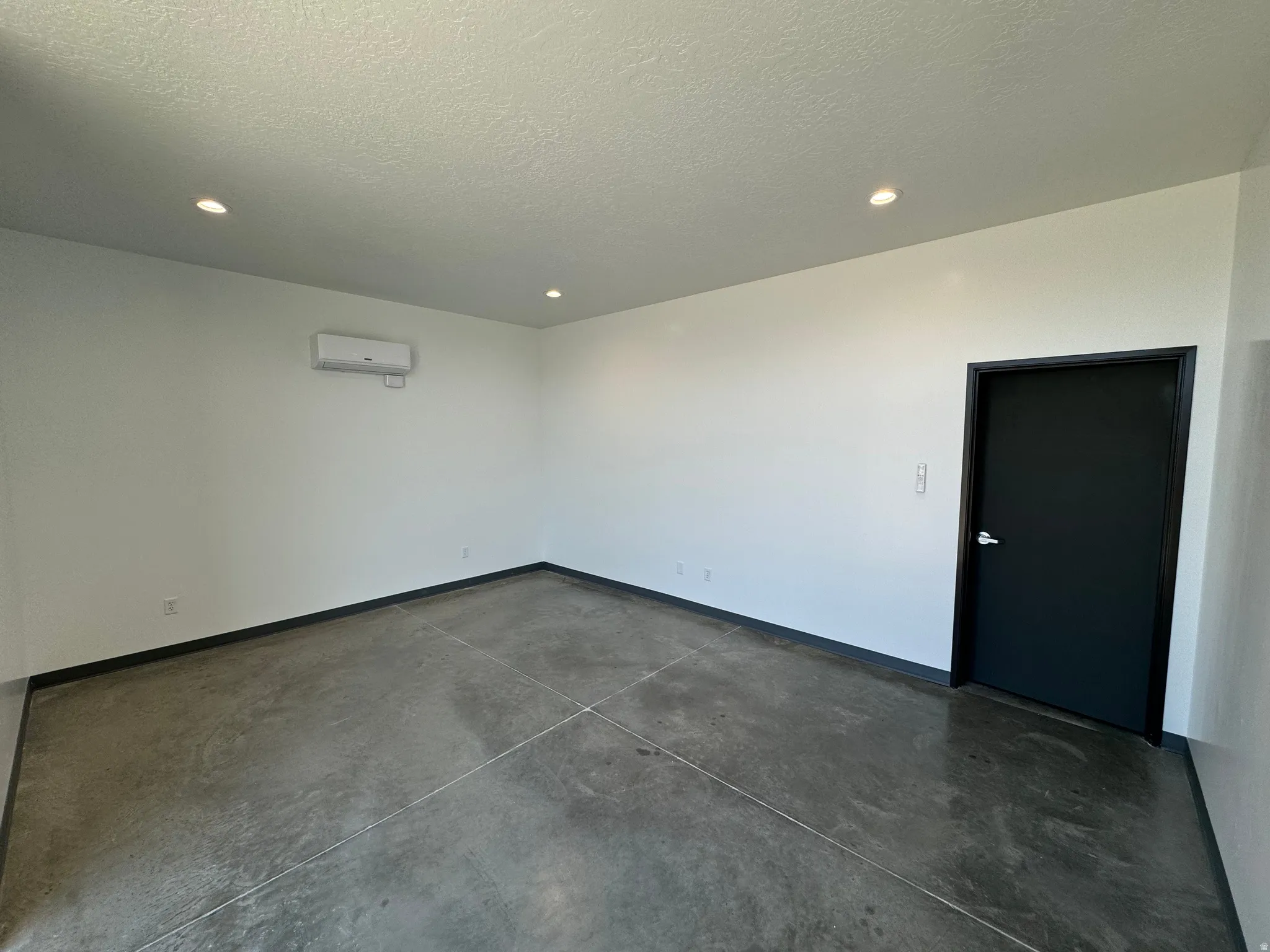 Spacious interior featuring concrete flooring, recessed lighting, white walls, and a black trim door