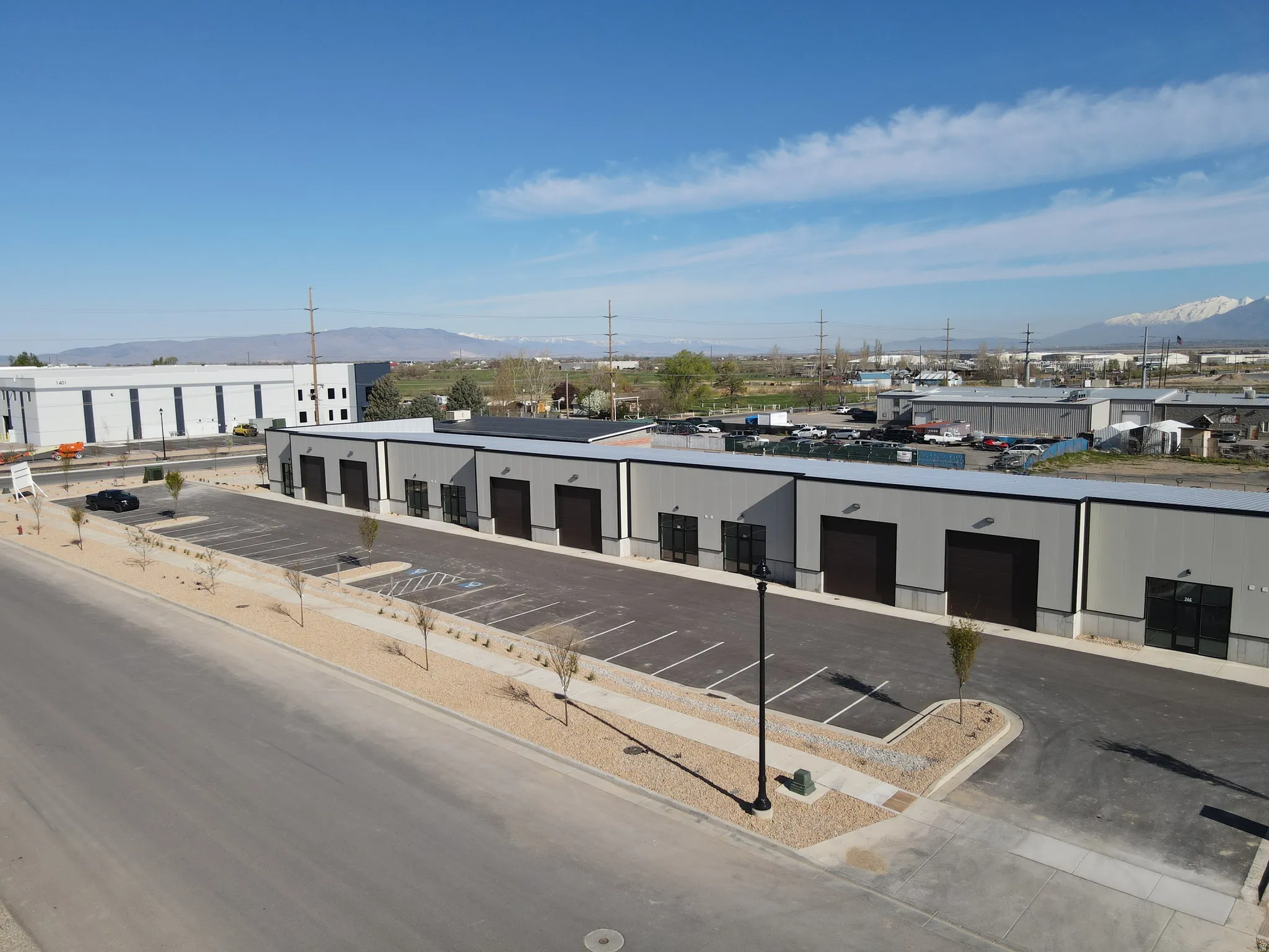 Commercial property featuring multiple bay doors, an expansive paved parking lot, and a gravel-landscaped frontage
