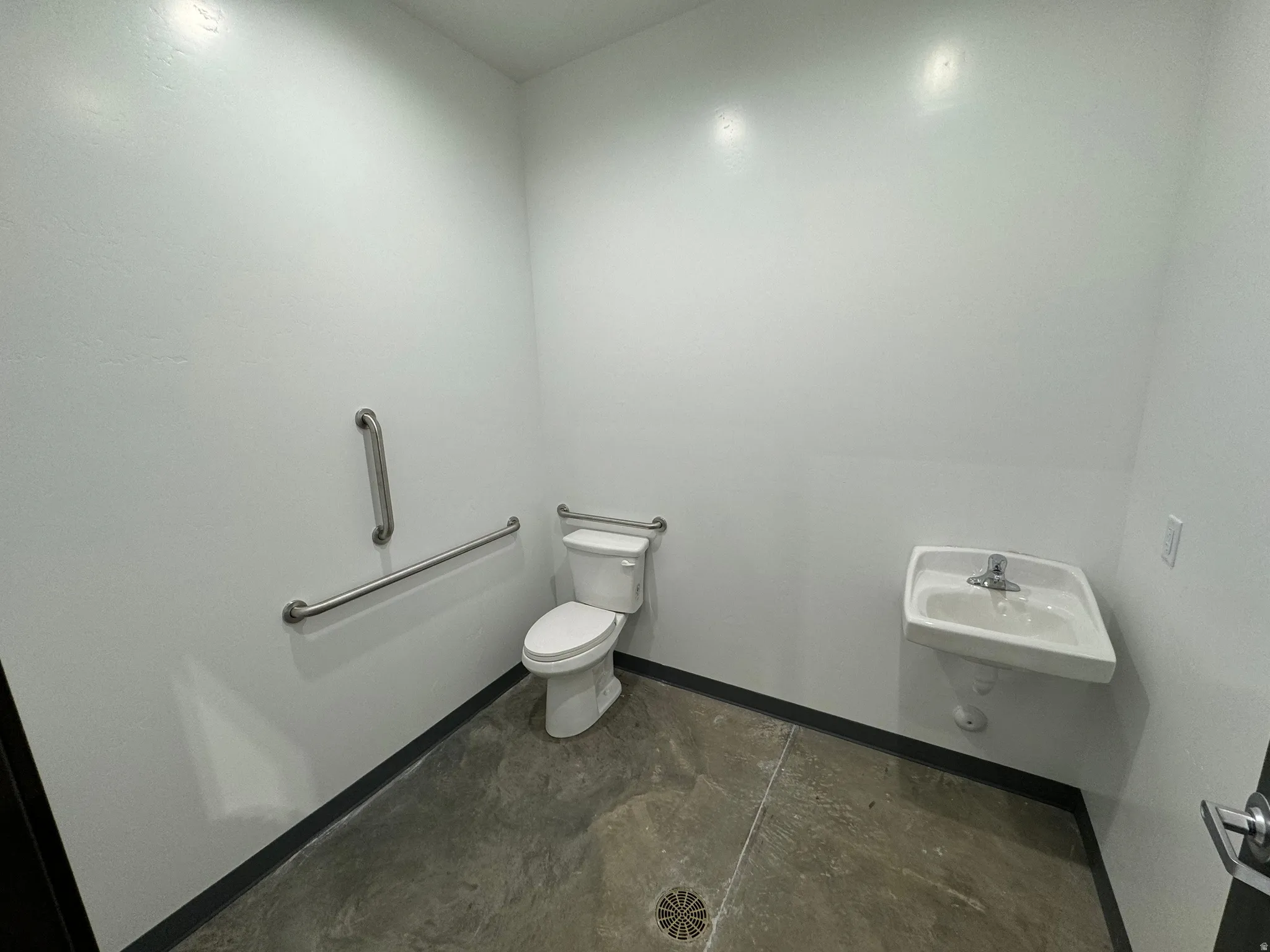Restroom with a wall-mounted sink, white toilet, and grab bars