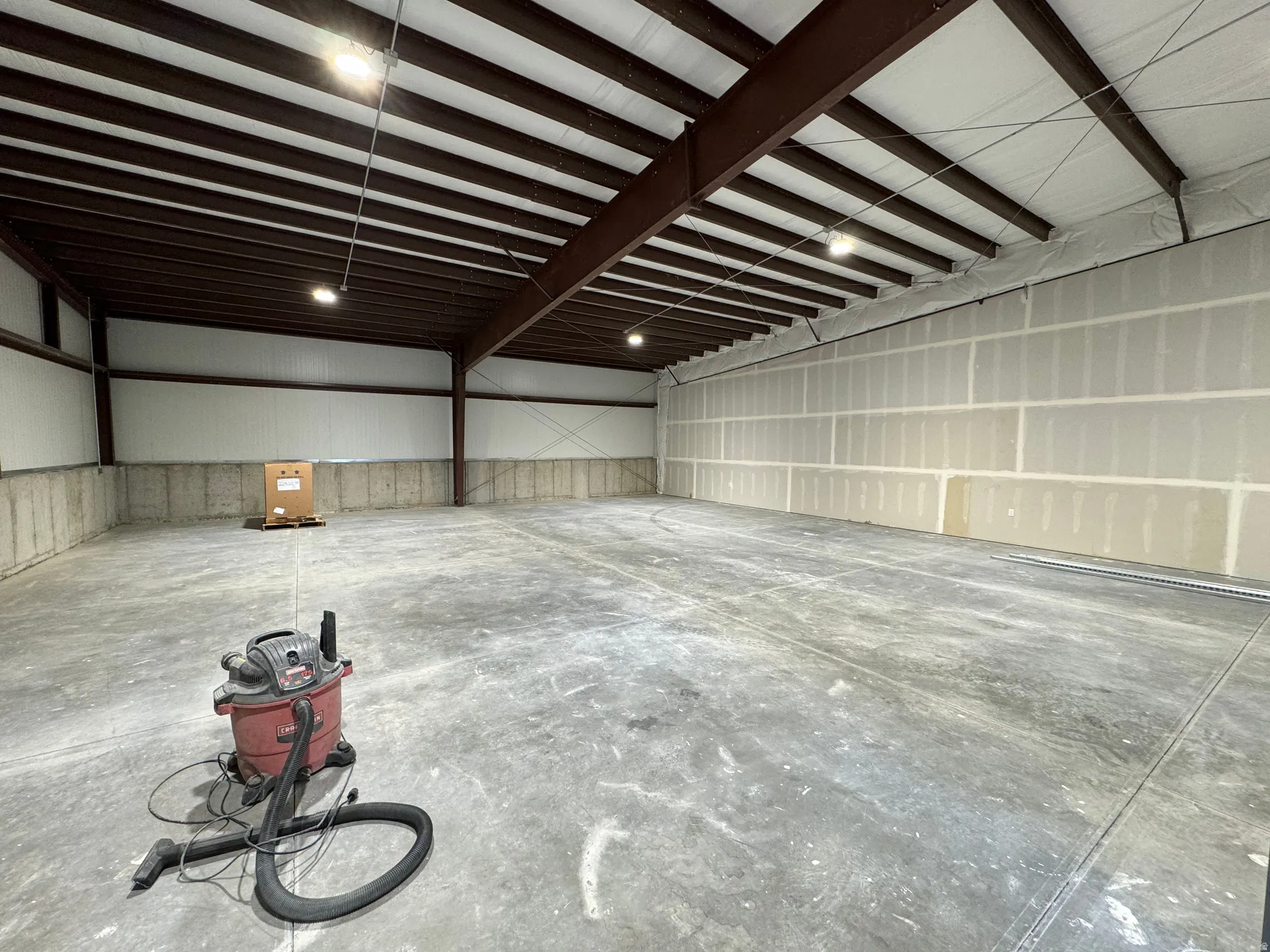 Expansive interior space featuring concrete flooring, steel beam construction, and high ceilings with industrial lighting