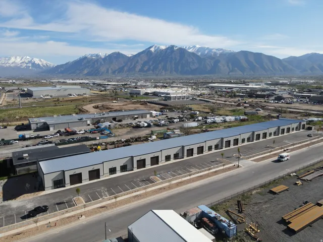 Industrial complex featuring multiple units with roll-up doors, paved parking areas, and a visible roadway