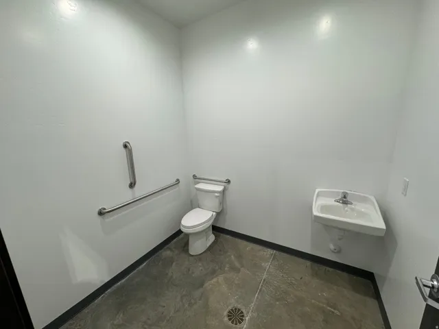 Restroom with a wall-mounted sink, white toilet, and grab bars
