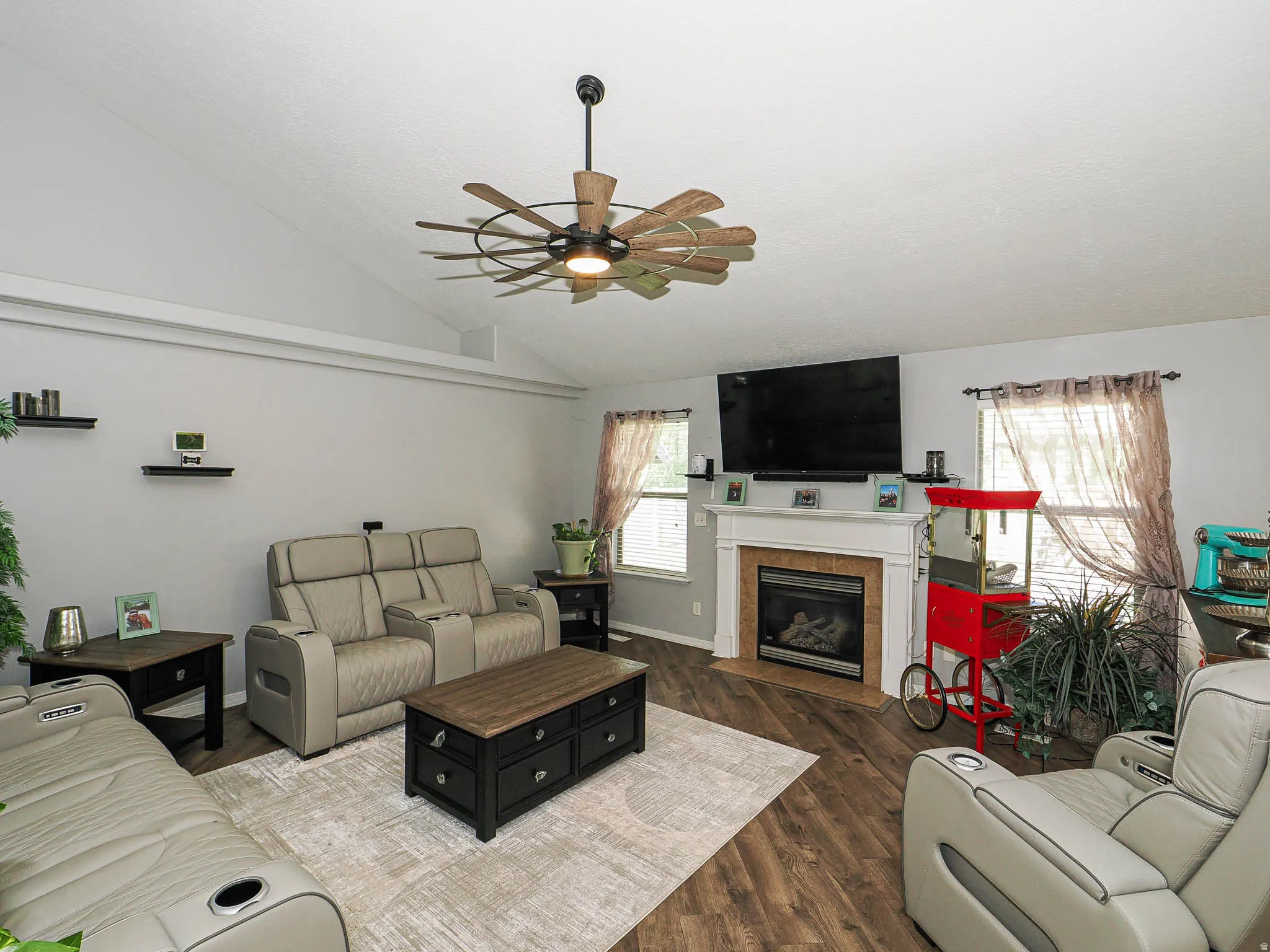 Spacious living area featuring a vaulted ceiling, wood-finish flooring, and a fireplace with a white mantel