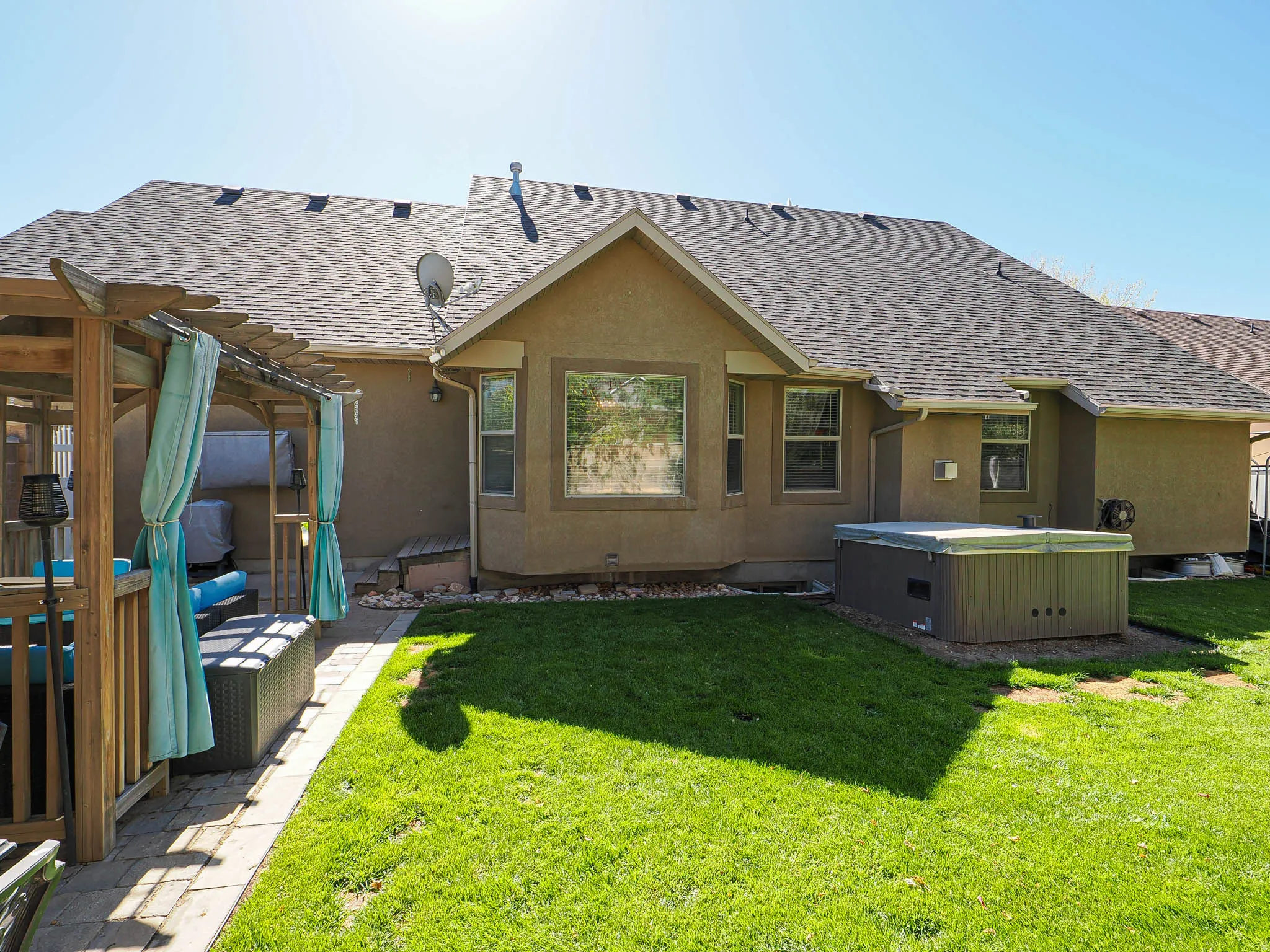 Expansive backyard featuring a manicured lawn, a built-in outdoor spa, a bay window, and a pergola with a paver patio