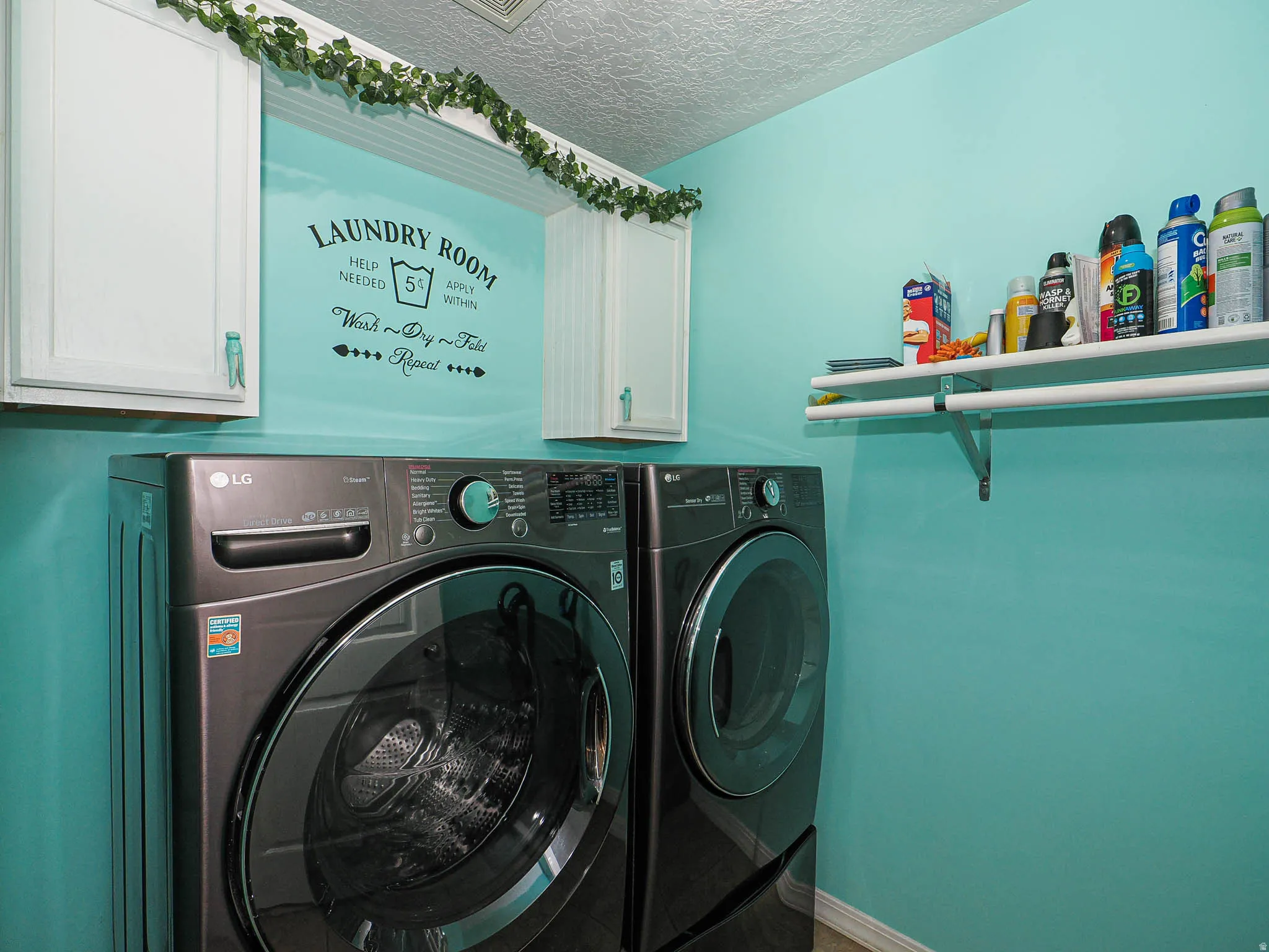 Dedicated laundry space featuring white upper cabinetry, a mounted shelving unit, and a textured ceiling
