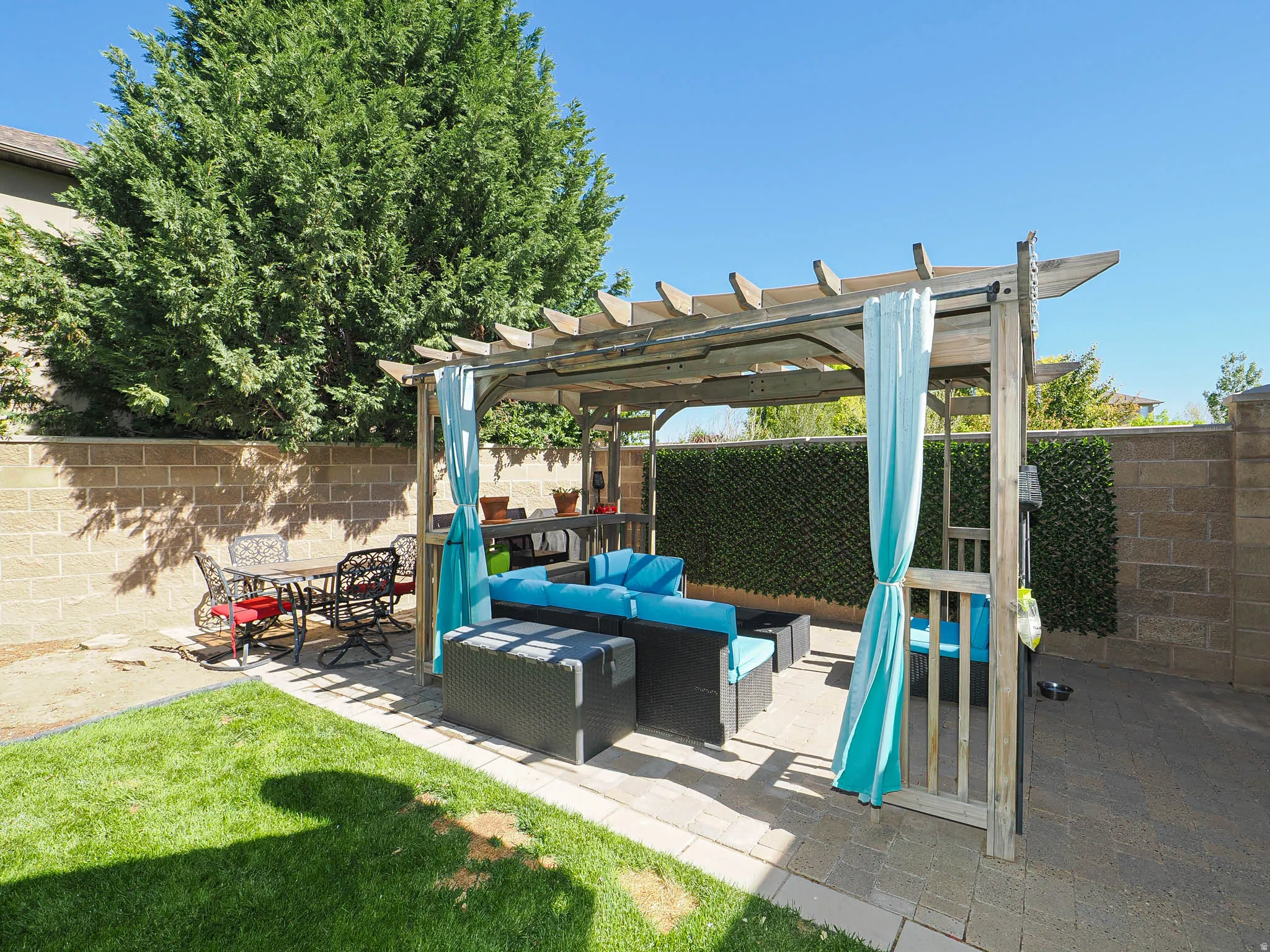 Backyard featuring a wooden pergola over a paver patio with an artificial hedge privacy wall