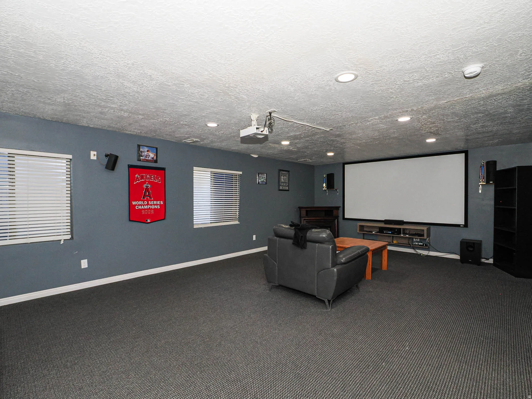 Spacious entertainment room featuring a large projection screen, recessed lighting, wall-mounted speakers, and a ceiling-mounted projector