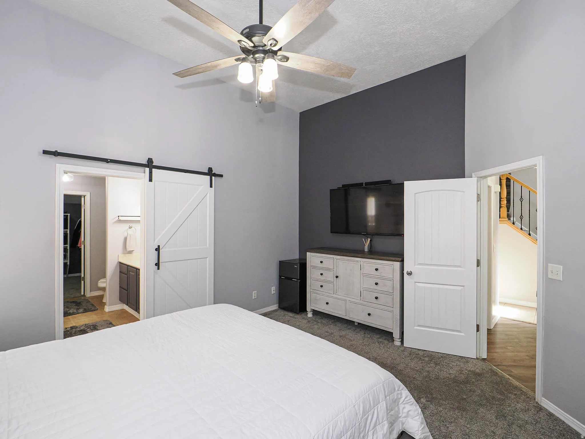 Vaulted ceiling with a ceiling fan, accent wall, barn door entry, and carpet flooring