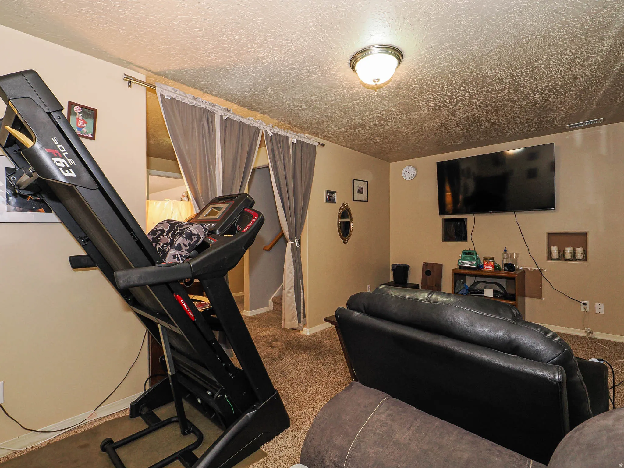 Carpeted interior space featuring a ceiling-mounted light fixture, built-in wall niches, and a wall-mounted television